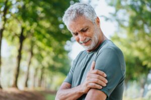 Homme qui se tient l'épaule à cause d'une douleur qui descend jusqu'au bras